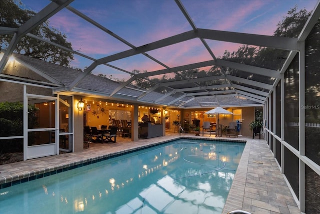 pool at dusk with a patio and glass enclosure