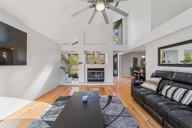 living room with hardwood / wood-style flooring, ceiling fan, high vaulted ceiling, and a tiled fireplace