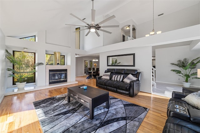 living room with hardwood / wood-style flooring, ceiling fan with notable chandelier, and high vaulted ceiling