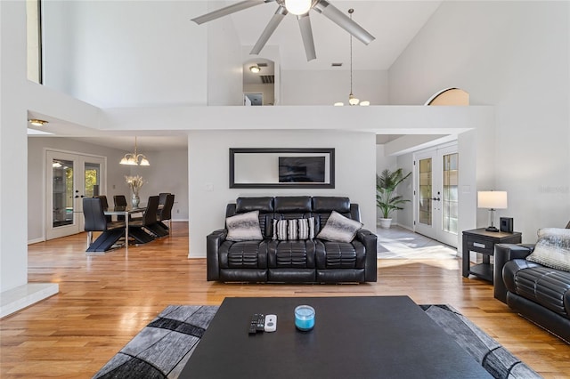 living room with french doors, high vaulted ceiling, ceiling fan with notable chandelier, and light wood-type flooring