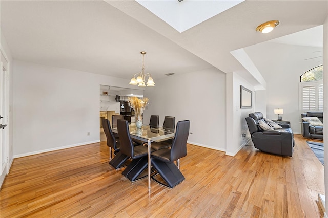 dining area featuring vaulted ceiling with skylight, a chandelier, and light hardwood / wood-style flooring