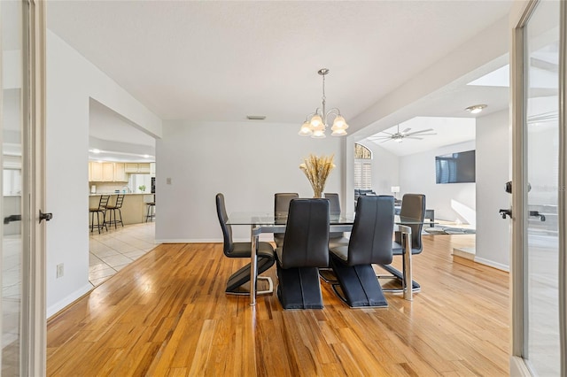 dining room with ceiling fan with notable chandelier, light wood-type flooring, vaulted ceiling, and a healthy amount of sunlight