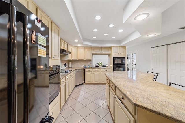 kitchen with black appliances, light stone counters, a breakfast bar area, and a tray ceiling