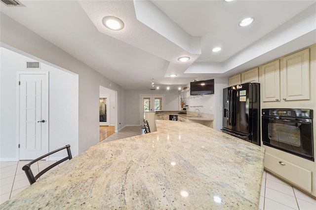 kitchen featuring sink, light stone counters, cream cabinets, a breakfast bar, and black appliances