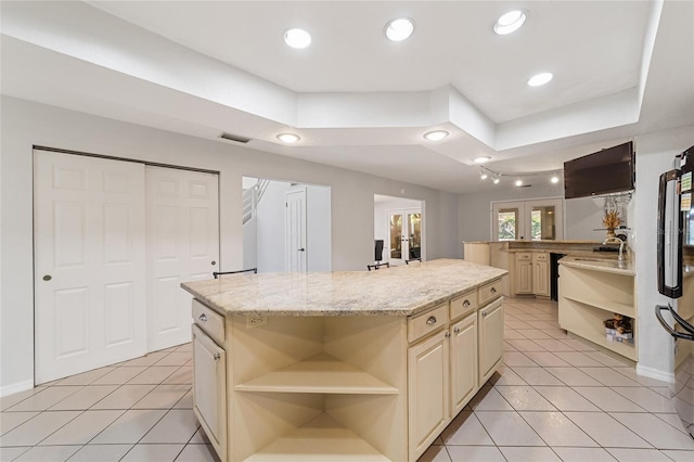 kitchen with a center island, french doors, light stone countertops, cream cabinetry, and light tile patterned flooring