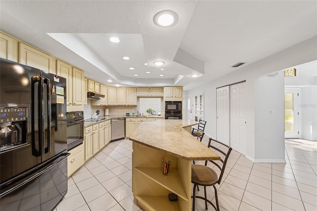 kitchen with light stone counters, a breakfast bar, a raised ceiling, black appliances, and a kitchen island