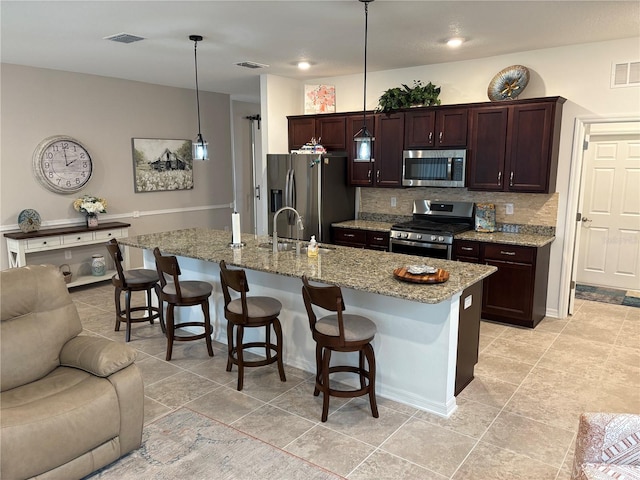 kitchen with a kitchen bar, a kitchen island with sink, pendant lighting, and stainless steel appliances