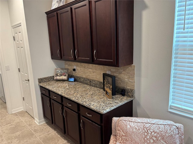 kitchen featuring decorative backsplash, dark brown cabinets, and light stone counters