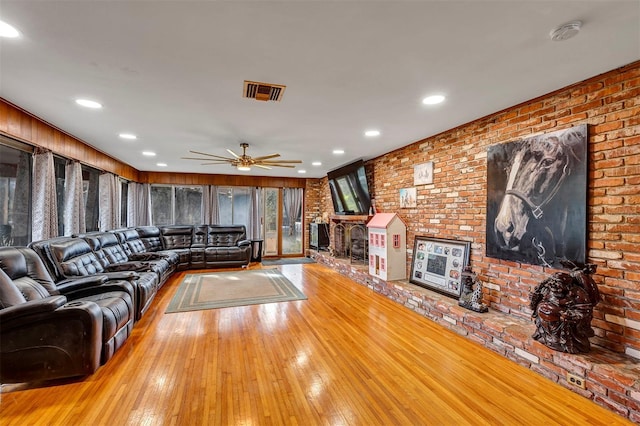 unfurnished living room with hardwood / wood-style floors, ceiling fan, and brick wall