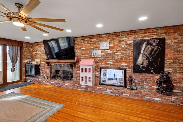 unfurnished living room with a fireplace, wood-type flooring, ceiling fan, and brick wall