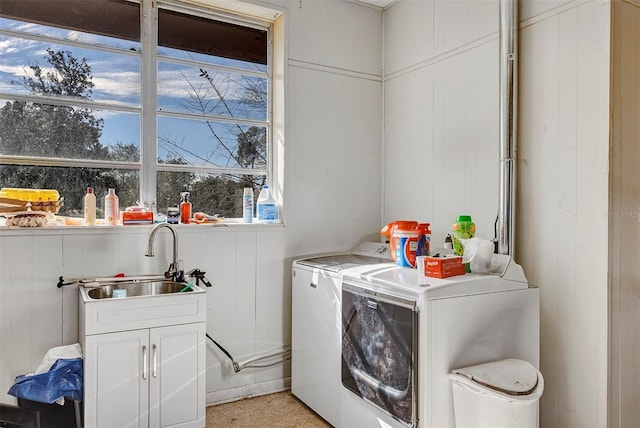 clothes washing area with wooden walls, sink, cabinets, and washer and dryer