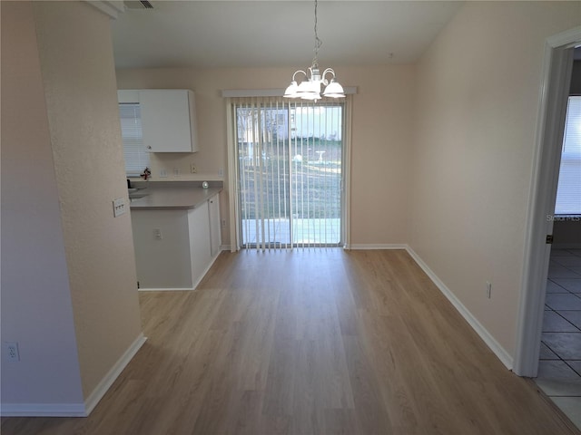 unfurnished dining area with a chandelier and light wood-type flooring