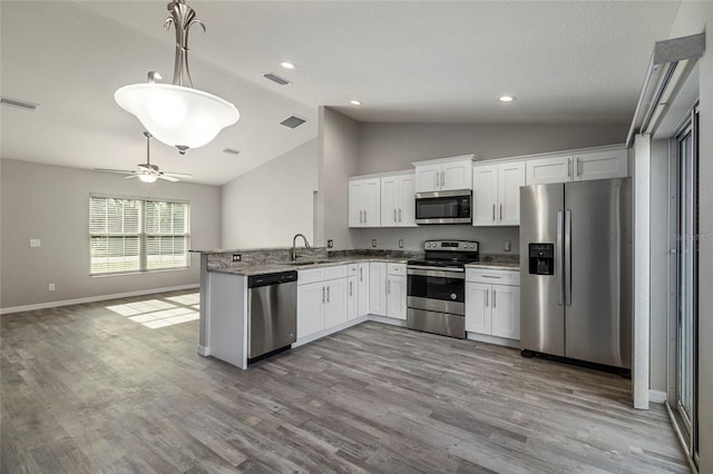 kitchen featuring appliances with stainless steel finishes, light wood-type flooring, decorative light fixtures, white cabinetry, and lofted ceiling