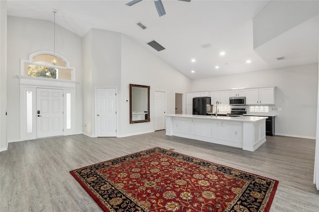 kitchen with white cabinets, stainless steel appliances, high vaulted ceiling, and a kitchen island with sink