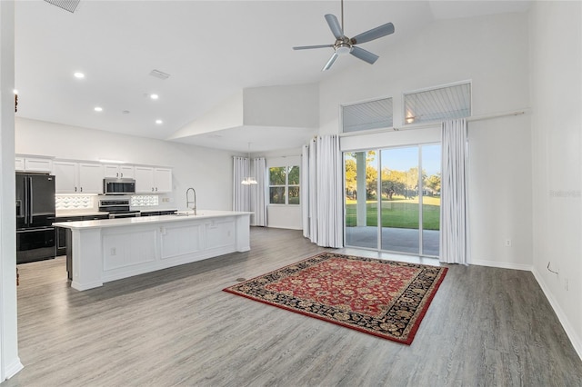 kitchen with appliances with stainless steel finishes, high vaulted ceiling, white cabinetry, and an island with sink