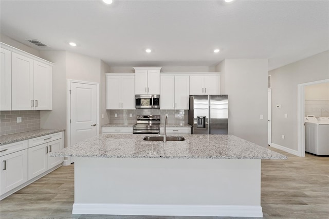 kitchen featuring a center island with sink, sink, stainless steel appliances, and washing machine and clothes dryer