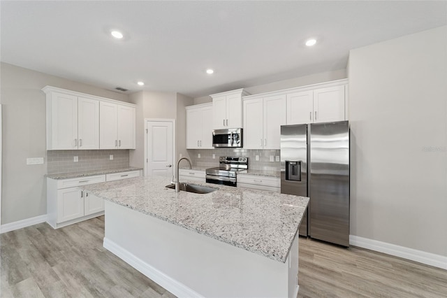 kitchen with appliances with stainless steel finishes, light wood-type flooring, sink, white cabinets, and an island with sink