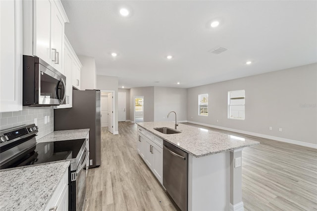 kitchen with light wood-type flooring, backsplash, stainless steel appliances, a center island with sink, and white cabinetry