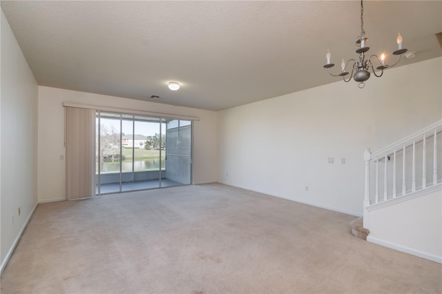 carpeted empty room with a textured ceiling and an inviting chandelier