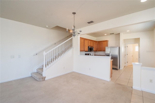 kitchen featuring kitchen peninsula, an inviting chandelier, light carpet, appliances with stainless steel finishes, and pendant lighting