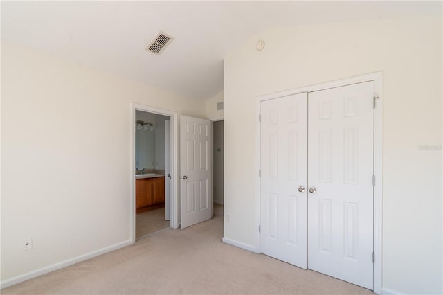 unfurnished bedroom with a closet, ensuite bath, vaulted ceiling, light carpet, and sink