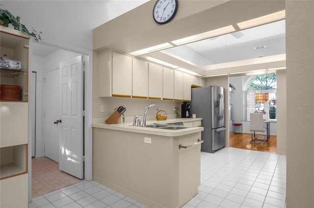 kitchen with kitchen peninsula, sink, a chandelier, white cabinetry, and stainless steel refrigerator