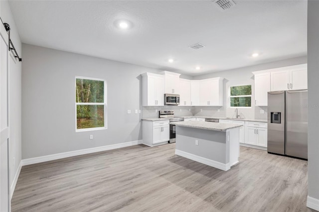 kitchen featuring a barn door, white cabinets, light wood-type flooring, and appliances with stainless steel finishes