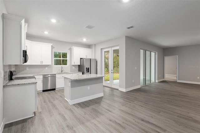 kitchen featuring black appliances, light hardwood / wood-style flooring, decorative backsplash, a kitchen island, and white cabinetry