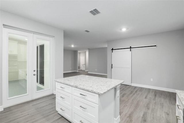 kitchen with light hardwood / wood-style floors, a barn door, light stone countertops, and white cabinetry