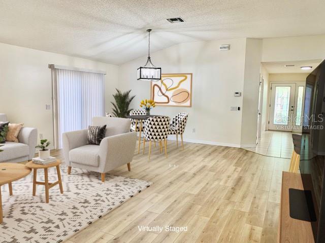 living room with a textured ceiling, light hardwood / wood-style flooring, a chandelier, and lofted ceiling