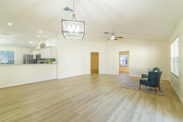 unfurnished room with ceiling fan with notable chandelier, vaulted ceiling, and light hardwood / wood-style flooring