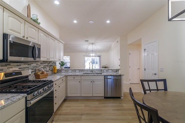 kitchen featuring kitchen peninsula, appliances with stainless steel finishes, light stone countertops, sink, and light hardwood / wood-style flooring