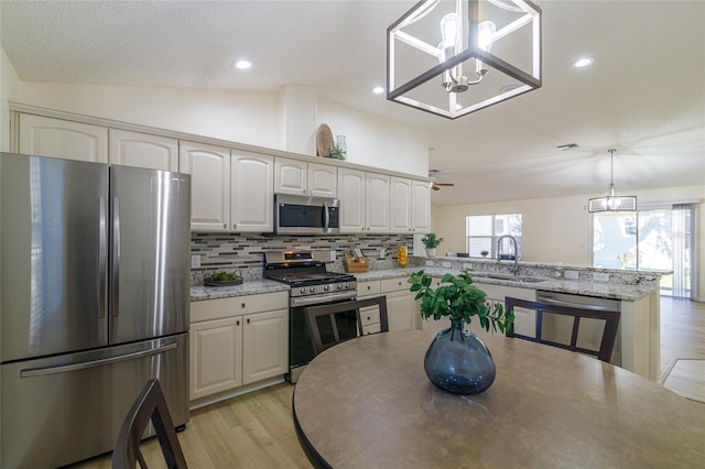 kitchen with light stone countertops, appliances with stainless steel finishes, vaulted ceiling, sink, and hanging light fixtures