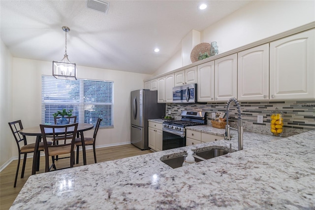 kitchen featuring light stone counters, backsplash, light hardwood / wood-style floors, pendant lighting, and appliances with stainless steel finishes