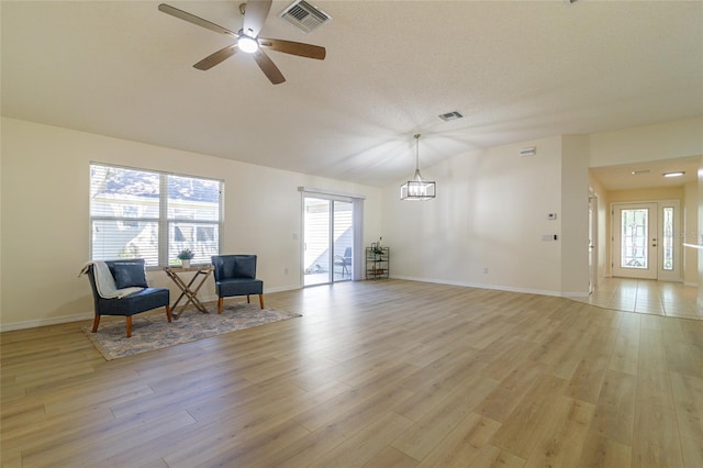 unfurnished room featuring lofted ceiling, a wealth of natural light, light hardwood / wood-style floors, and ceiling fan with notable chandelier