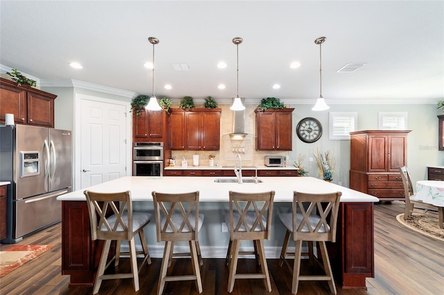 kitchen with a kitchen island with sink, wall chimney exhaust hood, hanging light fixtures, and appliances with stainless steel finishes