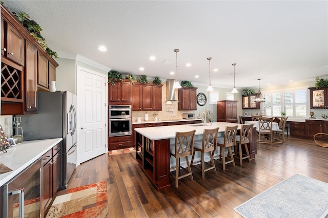 kitchen with an island with sink, wall chimney exhaust hood, pendant lighting, and dark hardwood / wood-style floors