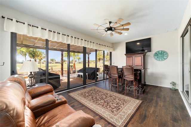 living room with bar area, ceiling fan, and dark wood-type flooring