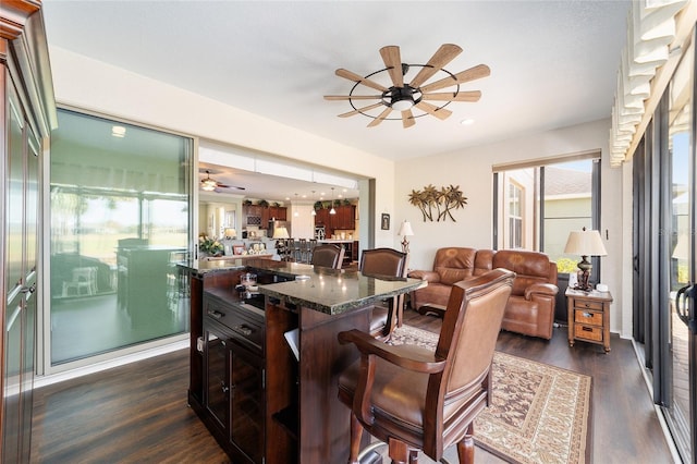 kitchen with dark stone counters, ceiling fan, a center island, dark hardwood / wood-style floors, and a breakfast bar area