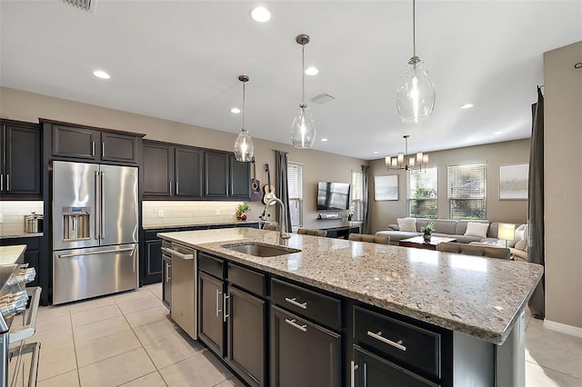 kitchen with sink, tasteful backsplash, an island with sink, decorative light fixtures, and appliances with stainless steel finishes