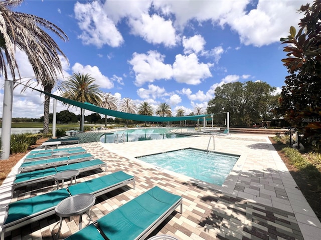 view of pool with a patio area, a water view, and a hot tub