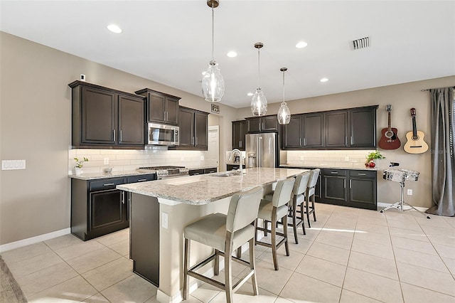 kitchen with appliances with stainless steel finishes, a breakfast bar, sink, pendant lighting, and a center island with sink