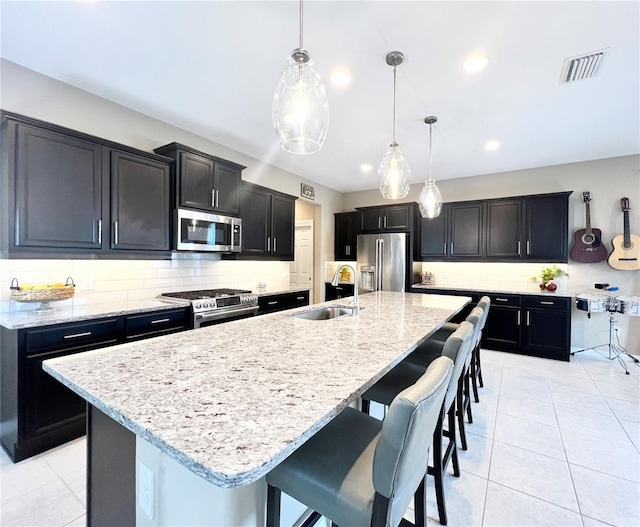 kitchen featuring sink, hanging light fixtures, an island with sink, tasteful backsplash, and stainless steel appliances