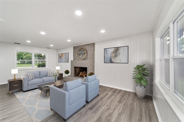 living room featuring crown molding, light hardwood / wood-style flooring, wooden walls, and a brick fireplace