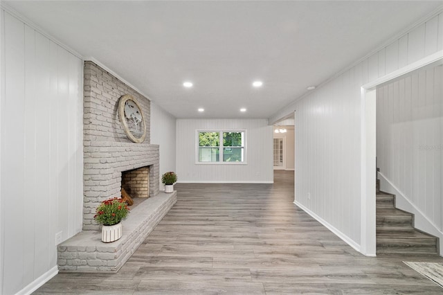 unfurnished living room with a fireplace, wooden walls, light hardwood / wood-style flooring, and ornamental molding