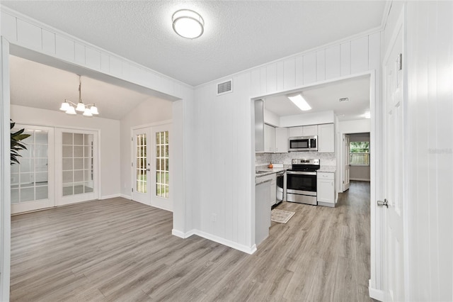 kitchen with pendant lighting, french doors, white cabinets, appliances with stainless steel finishes, and light hardwood / wood-style floors