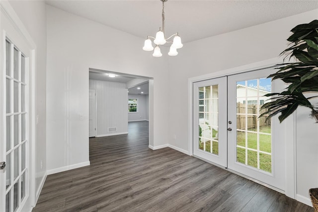 unfurnished dining area with a notable chandelier, dark hardwood / wood-style flooring, a textured ceiling, and french doors