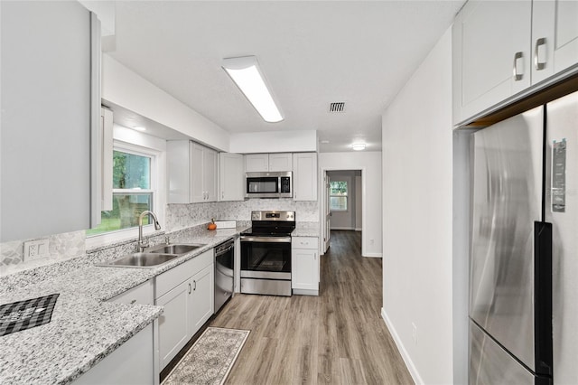 kitchen with sink, stainless steel appliances, light stone counters, backsplash, and light wood-type flooring