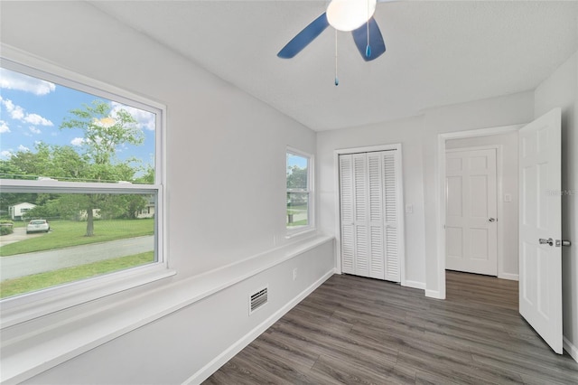 unfurnished bedroom with multiple windows, ceiling fan, a closet, and dark hardwood / wood-style floors