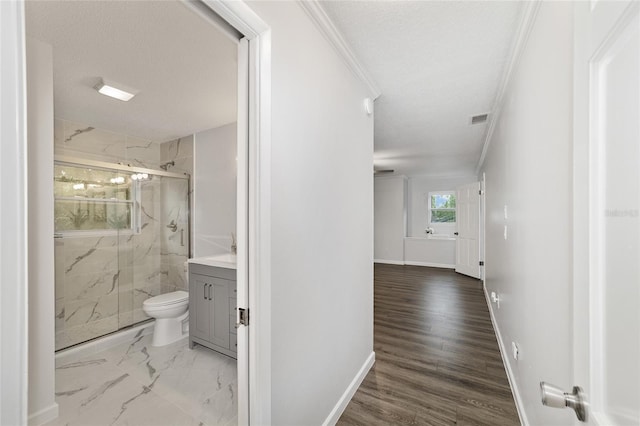 corridor with a textured ceiling, wood-type flooring, and crown molding